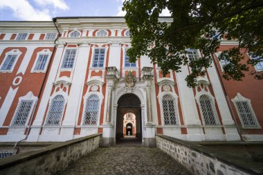 Broumov Manastırı. Süslü kırmızı ve beyaz bir cephe ve kemerli bir giriş kapısı var.