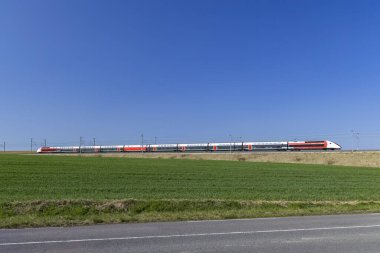 Yüksek hızlı yolcu treni, açık mavi gökyüzünün altındaki yeşil arazide hızla ilerliyor.