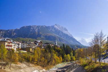 Alp kilisesi çan kulesi olan köy panoraması ve dağ zirvelerine karşı renkli sonbahar yaprakları.