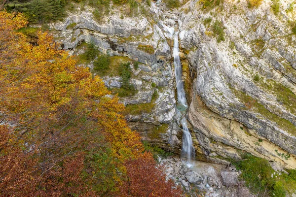 Slovenya 'nın Bovec kentinde çağlayan şelale, canlı sonbahar yapraklarıyla kaplı katmanlı kayaların arasından akıyor.