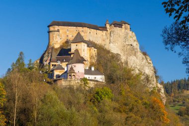 Orava Kalesi, ortaçağ kale mimarisi sonbahar ağaçlarıyla çevrili bir kaya uçurumunda.