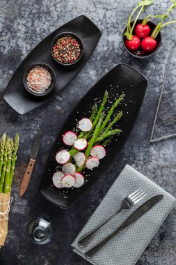 Sağlıklı kuşkonmaz ve turp salatası koyu bir arka planda baharatlarla servis ediliyor.