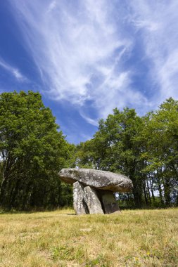 Megalitik dolmen yapısı mavi gökyüzünün altında çimenli bir alanda duruyor.