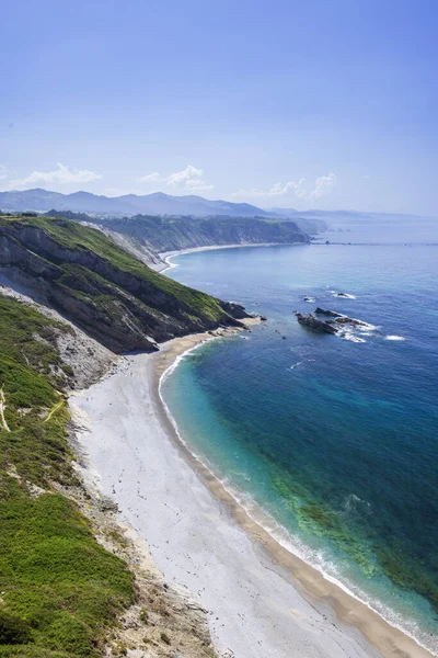 Engebeli bir kıyı şeridi, çakıl taşı plajı ve canlı mavi okyanus sularının manzarası.