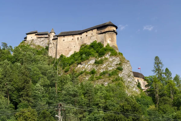Orava Kalesi, açık bir gökyüzünün altındaki yemyeşil bir ormana bakan yüksek bir kayanın üzerine inşa edilmiş bir ortaçağ kalesi.