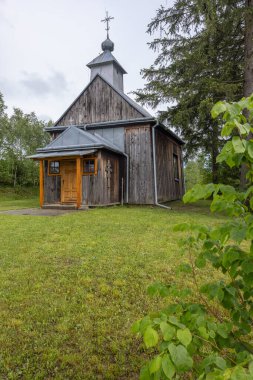Tarihi ahşap kilise bulutlu bir gökyüzünün altında yeşil çimlerin ve ağaçların arasında duruyor.