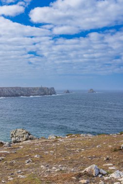 Bulutlu bir gökyüzünün altında deniz feneri, uçurum ve okyanusla kaplı engebeli Brittany kıyıları