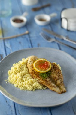 Kuskus, limon dilimi ve kırmızı havyarla servis edilen ızgara balık filetosu.