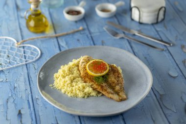 Kuskus, limon dilimi ve kırmızı havyarla servis edilen tavada kızarmış balık filetosu.