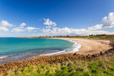 Temiz turkuaz suyu, kayaları, kumları ve mavi gökyüzü olan sahili.