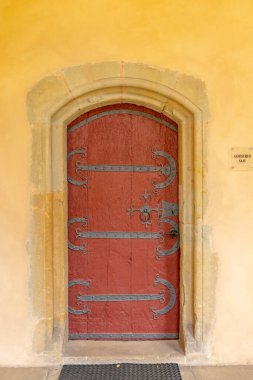 Ağaçlardaki tarihi bir kemerli taş kapıya demirden menteşeleri olan kırmızı ahşap kapı.