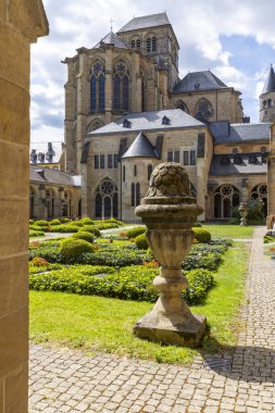 Tarihi Trier Katedrali Manastır Bahçesi. Mavi gökyüzünün altında manikürlü çalılar ve antik taş vazo sergileniyor.