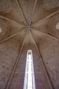Stone vaulted ceiling arching towards a tall, narrow arched window filling the space with light