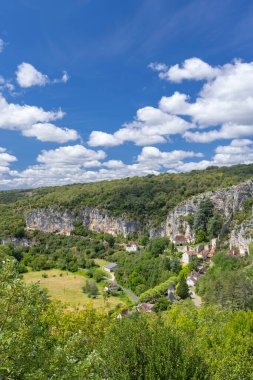 Mavi gökyüzünün altında dramatik uçurumların altında yeşil vadiyi noktalayan tarihi evler.