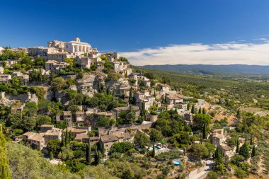 Gordes köyü binaları Provence 'deki açık mavi gökyüzünün altında kayalık bir tepeye tırmanıyor.