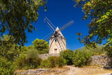 Provence 'deki açık mavi gökyüzünün altında yeşil ağaçların çerçevelediği tarihi yel değirmeni.