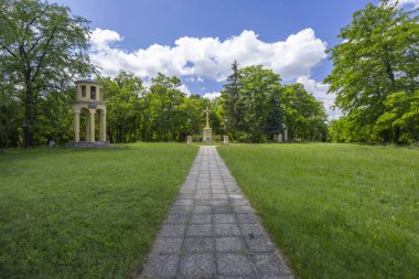 Yeşil ağaçlar ve otlarla çevrili dini bir haça ve kubbeye giden yol.