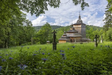 Antik ahşap ortodoks kilisesi mavi çiçekler ve ormanlı yeşil bir çayırda duruyor.