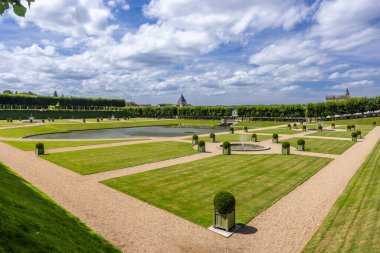Manikürlü çalılar, yeşil çimenler, göletler ve bulutlu bir gökyüzünün altındaki çeşmeler içeren zarif Fransız bahçeleri.