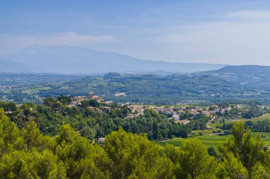 Köy yeşil tepelerin ve üzüm bağlarının arasına kurulmuş. Mavi gökyüzünün altındaki uzak dağlar, Vinsobres.