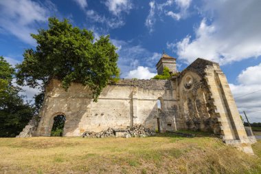 Eski taş kilise kalıntıları mavi bir gökyüzünün altında duruyor, yemyeşil ağaçlarla kaplanmış.