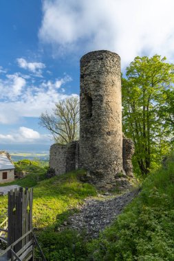 Antik taş kale kulesi parlak mavi gökyüzünün altında çimenli bir tepenin üzerinde duruyor.