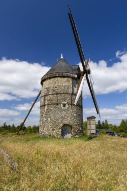 Eski taş değirmeni Moulin de La Roche mavi gökyüzünün altında kuru bir tarlada duruyor.