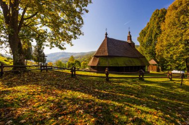 Güneşli bir günde, sonbahar yaprakları ve tepelerle çevrili eski ahşap kilise.