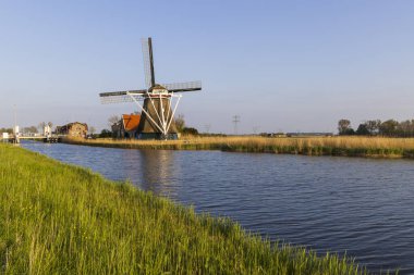 Geleneksel Hollanda yel değirmeni De Lastdrager yeşil çimlerle çevrili bir kanalda duruyor