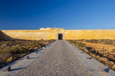 Portekiz bayraklı Sagres Kalesi girişi açık mavi gökyüzünün altında dalgalanıyor