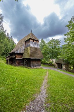 Slovakya 'nın Zuberec kentindeki tarihi ahşap kilise binası bulutlu gökyüzünün altındaki ağaçların arasında duruyor.