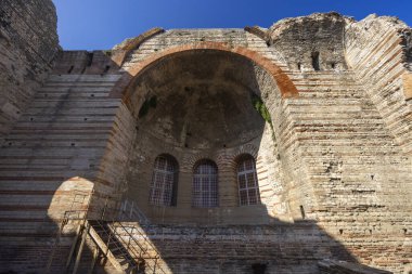 Antik Roma hamamı, berrak mavi gökyüzü altında kavisli oyuklar ve tuğla işleriyle harabeler.