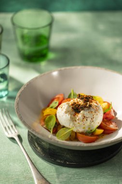 Yumuşak burrata peyniri, canlı domates salatası ve fesleğenle servis edilir.
