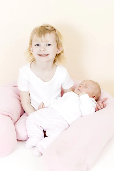 Porträt eines kleinen Mädchens, das seine einen Monat alte kleine Schwester wiegt — Stockfoto