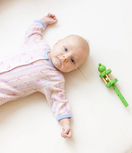 Liegen een twee maanden oude babymeisje met een rammelaar — Stockfoto