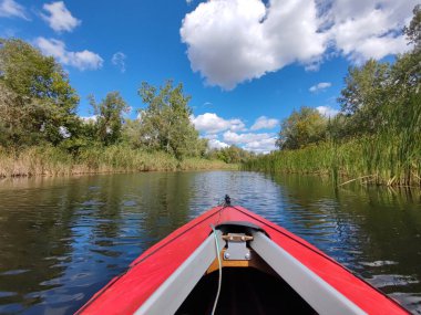 Gökyüzündeki bulutların altında küçük bir nehirde kırmızı kano.