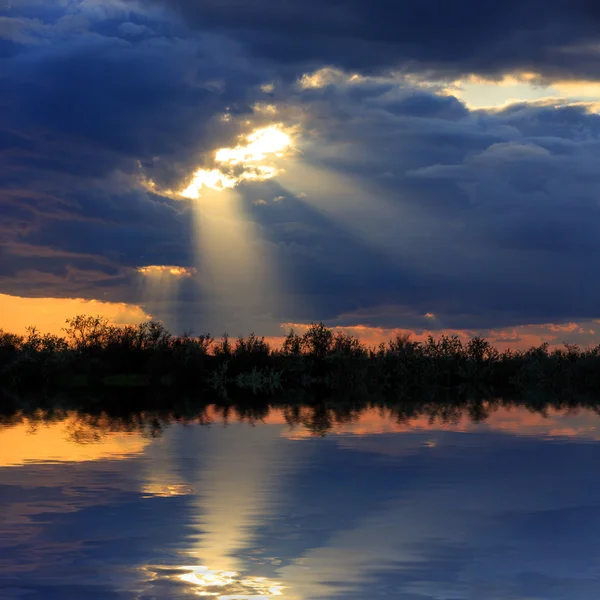 Темные облака с солнечными лучами над озером — стоковое фото