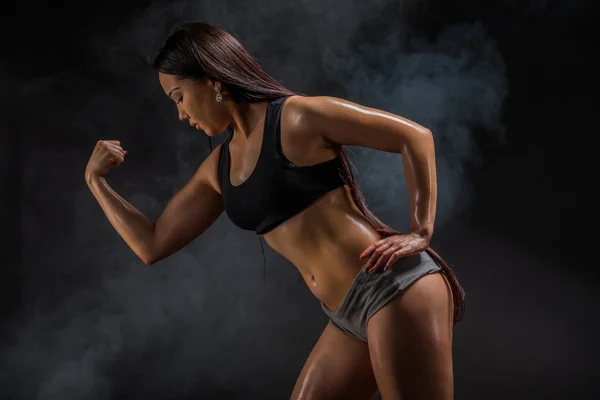 Молода м'язиста жінка позує на чорному — стокове фото