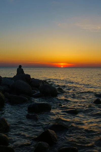 Homme assis sur les pierres au bord de la mer — Photo