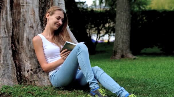 Молодая женщина читает книгу в парке — стоковое видео