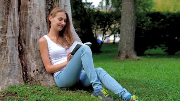 Junge Frau liest im Park ein Buch — Stockvideo