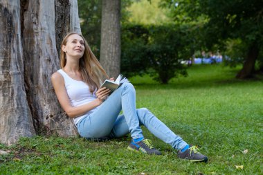 Genç bir kadın parkta kitap okuyor.