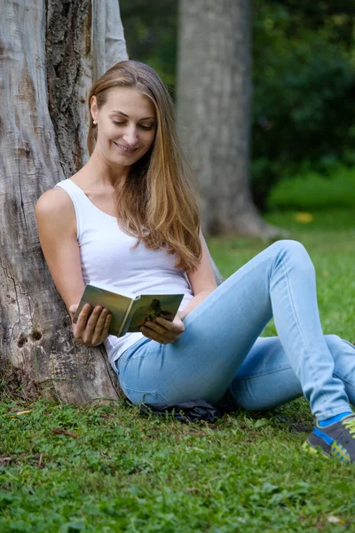 Genç bir kadın parkta kitap okuyor. — Stok fotoğraf