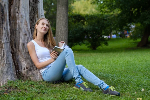 Genç bir kadın parkta kitap okuyor. — Stok fotoğraf