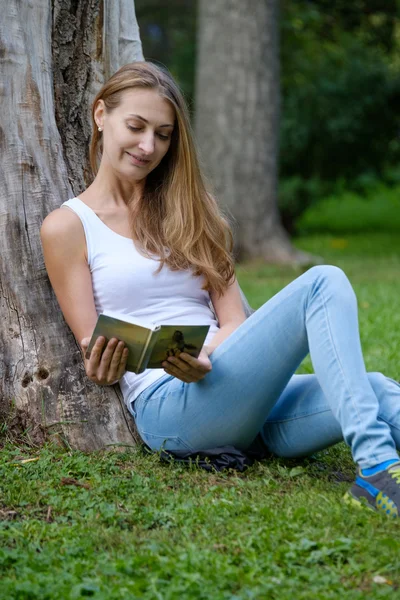 公園で本を読んでいる若い女性が — ストック写真