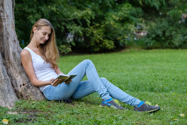 公園で本を読んでいる若い女性が — ストック写真