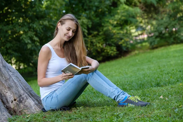 Mladá žena čte knihu v parku — Stock fotografie