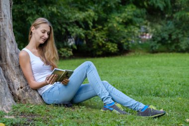 Genç bir kadın parkta kitap okuyor.