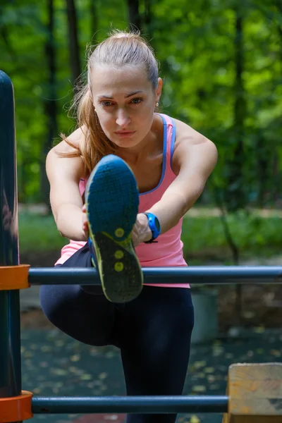 Jeune femme mince étirant dans un terrain d'entraînement — Photo