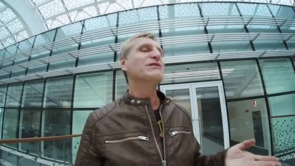 Männlicher Reisender spricht in modernem Gebäude vor laufender Kamera — Stockvideo